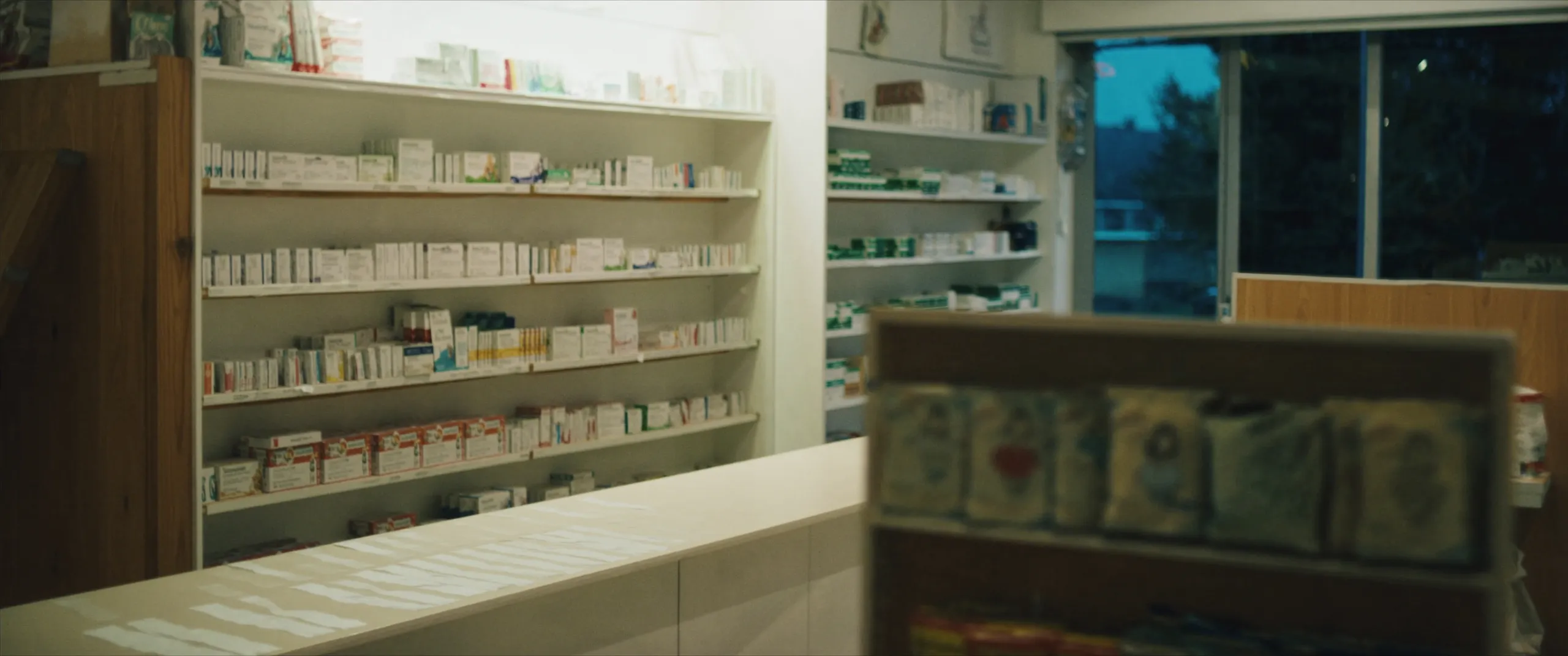 L’intérieur d’une officine juste après la fermeture, rayonnages et comptoir dans la lumière du soir.